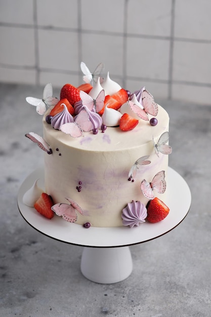 Beautiful and delicate strawberry cake for a girl. Dessert is decorated with fresh strawberries, meringues and butterflies.