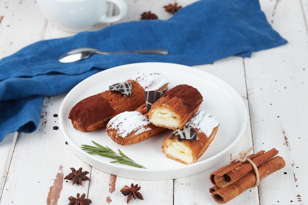 Beautiful delicious french eclairs set with original cream decor on white plate on wooden background tasty colorful dessert profiteroles