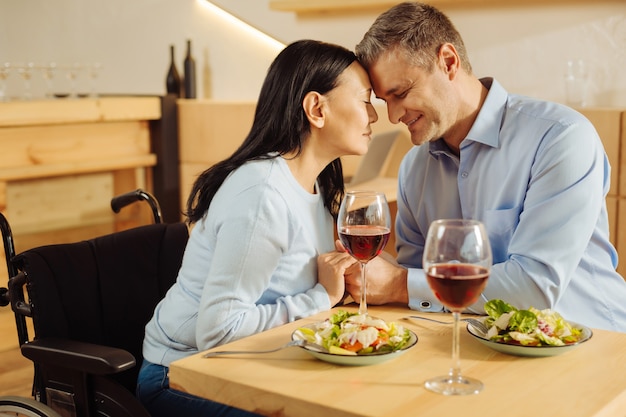 目を閉じて手をつないでカフェに座って夕食をとっている美しい喜んでいる障害のある女性と魅力的なインスピレーションを得たしっかりした男