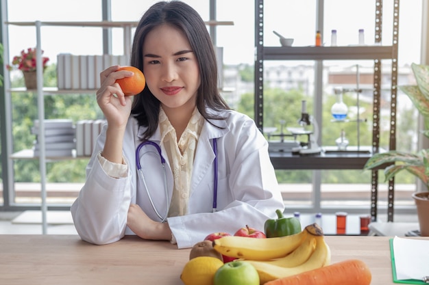 Beautiful doctor showing an orange in the office