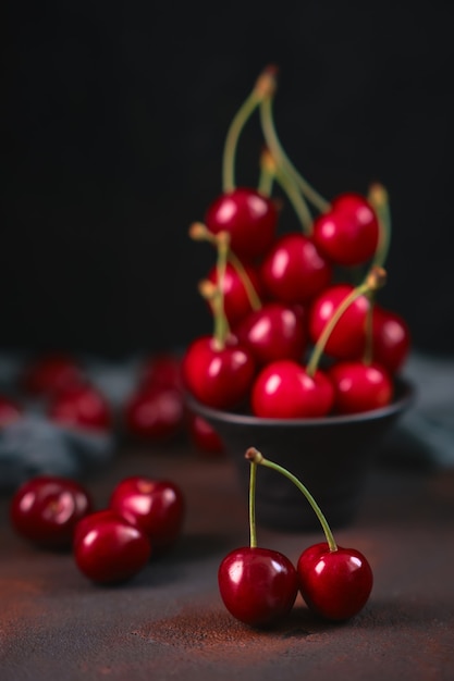 Beautiful double cherry in the foreground and Fresh and sweet red cherries in a black earthenware bowl on a dark surface with water drops. seasonal fruit, delicacy