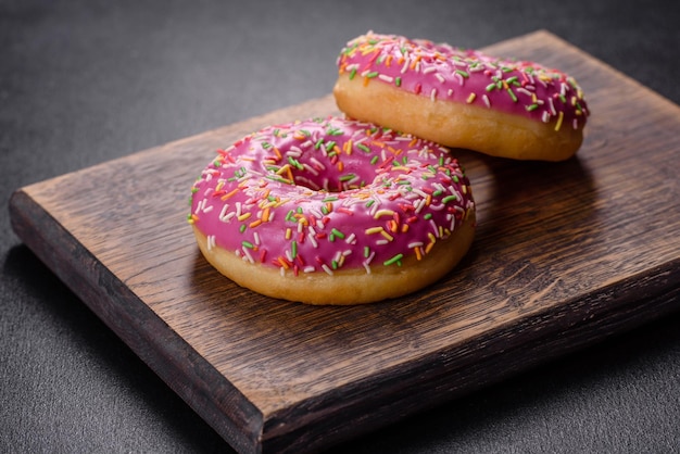 A beautiful doughnut with pink glaze and colored sprinkle on a dark concrete background