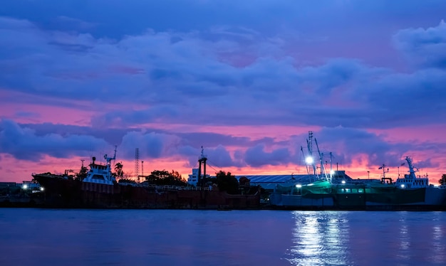 Beautiful dramatic twilight sky over nautical vessel at harbor\
in industrial area along the river