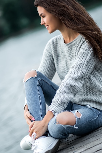 Beautiful dreaming woman sitting on pier by the lake.