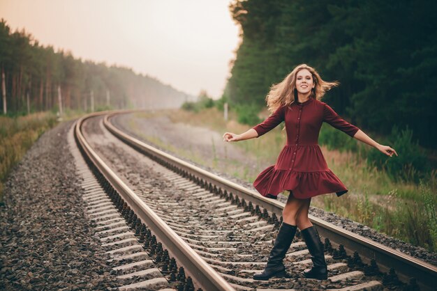 Beautiful dreamy woman in crimson dress enjoy nature in forest on railway