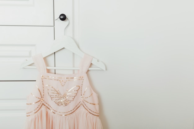 Beautiful dressy lush pink dress for girls on hanger at the background of white wardrobe.