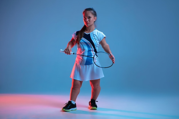 Beautiful dwarf woman practicing in badminton isolated on blue background in neon light