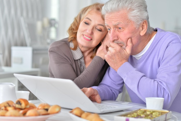 Beautiful elderly couple having breakfast with laptop