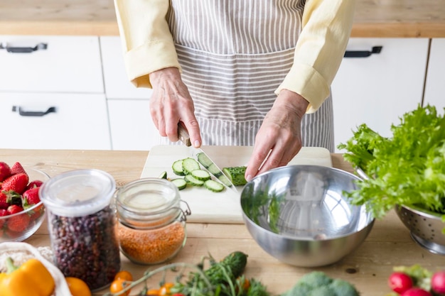 Beautiful elderly gray haired senior woman cook in cozy kitchen with fresh organic vegetables tomatoes cabbage lettuce cucumbers on table cooking healthy vegetable salad healthy food active life