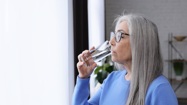 사진 물 잔을 들고 마시는 아름 다운 노인 회색 머리 여자.