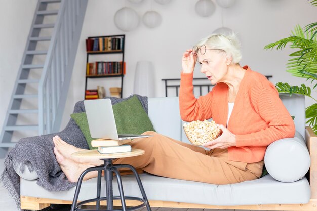 Photo beautiful elderly senior woman in cosy apartment works on laptop beautiful gray haired woman works online or watching movie studies and communicates concept of active old age