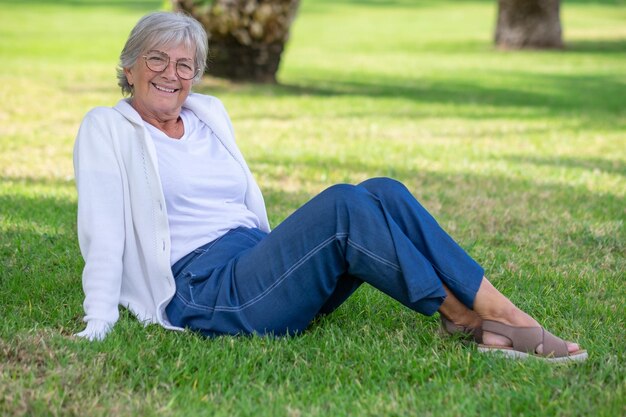 Beautiful elderly woman gray haired sitting in the meadow smiling and relaxing