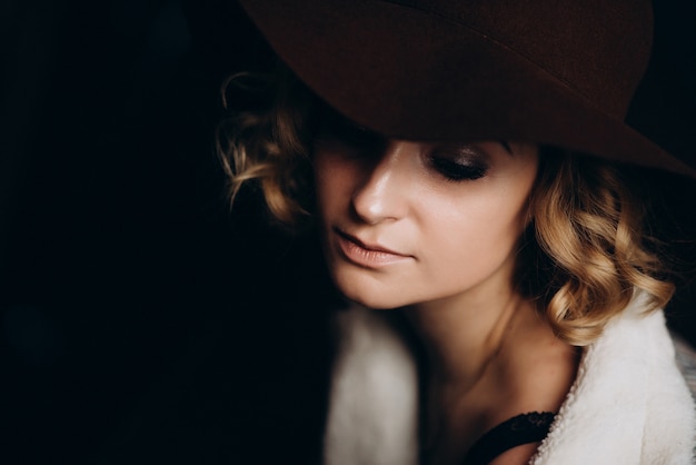 Bella ragazza bionda elegante in un cappello su un'oscurità