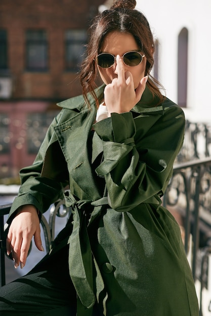 Bella donna elegante del brunette che porta cappotto verde sul balcone