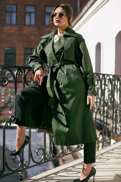 Beautiful elegant brunette woman wearing green coat on the balcony