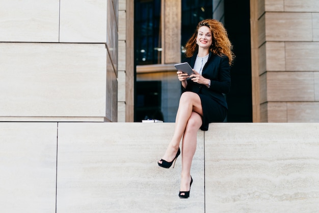 Beautiful elegant businesswoman in formal clothes and high-heeled shoes, having wavy hair and slender legs