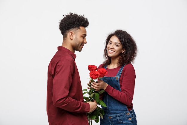 Красивая элегантная пара обнимает и улыбается, на сером фоне. Девушка держит розы