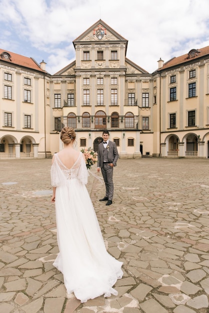 Beautiful elegant couple of newlyweds in love on the background of an old building and paving stones European wedding