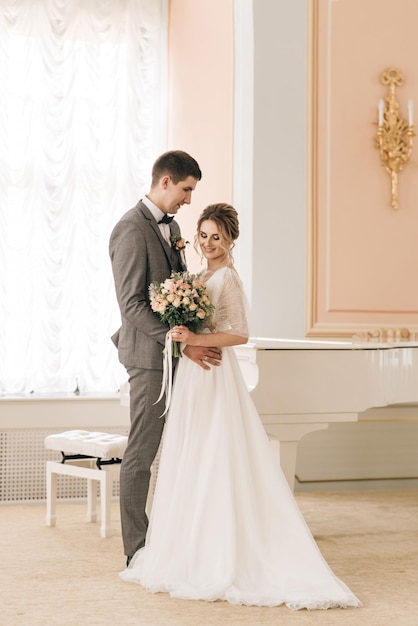 Beautiful elegant couple of newlyweds in love in a luxurious interior near the piano