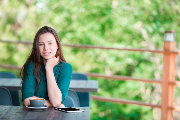 Beautiful elegant girl having breakfast at outdoor cafe. Happy young urban woman drinking coffee