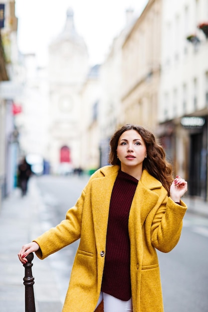 Beautiful elegant girl in a yellow coat walks through the streets of Paris