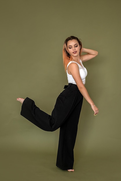 Beautiful and elegant lady in black clothes stands near the green wall The concept of a beautiful girl