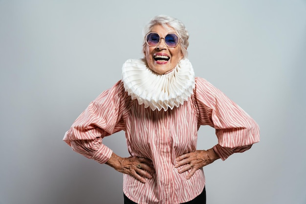 Beautiful and elegant old influencer woman. Cool grandmother posing in studio wearing fashionable clothes. Happy senior lady celebrating and making party. Concept about seniority and lifestyle