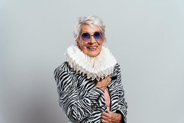 Beautiful and elegant old influencer woman. Cool grandmother posing in studio wearing fashionable clothes. Happy senior lady celebrating and making party. Concept about seniority and lifestyle