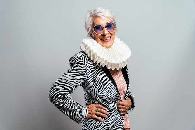 Beautiful and elegant old influencer woman. Cool grandmother posing in studio wearing fashionable clothes. Happy senior lady celebrating and making party. Concept about seniority and lifestyle