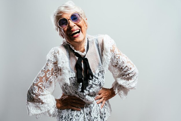 Beautiful and elegant old influencer woman. Cool grandmother posing in studio wearing fashionable clothes. Happy senior lady celebrating and making party. Concept about seniority and lifestyle