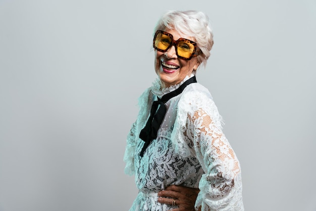 Beautiful and elegant old influencer woman. Cool grandmother posing in studio wearing fashionable clothes. Happy senior lady celebrating and making party. Concept about seniority and lifestyle