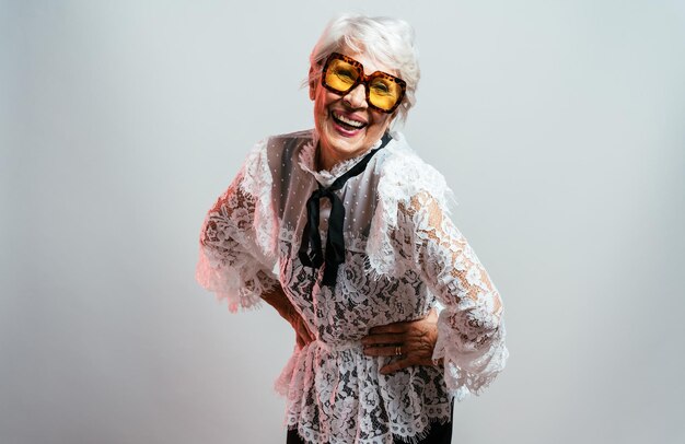 Beautiful and elegant old influencer woman. Cool grandmother posing in studio wearing fashionable clothes. Happy senior lady celebrating and making party. Concept about seniority and lifestyle