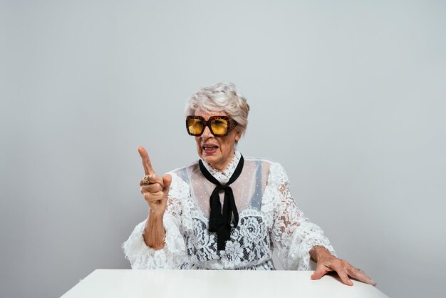 Beautiful and elegant old influencer woman. Cool grandmother posing in studio wearing fashionable clothes. Happy senior lady celebrating and making party. Concept about seniority and lifestyle