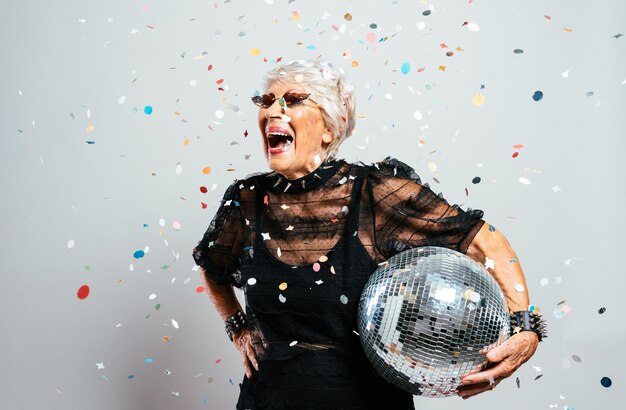 Beautiful and elegant old influencer woman. Cool grandmother posing in studio wearing fashionable clothes. Happy senior lady celebrating and making party. Concept about seniority and lifestyle