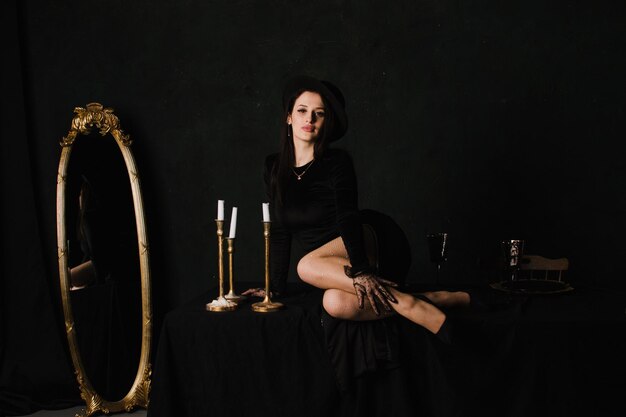 Красивая элегантная женщина в перчатках и платье сидит на столе на черном фоне