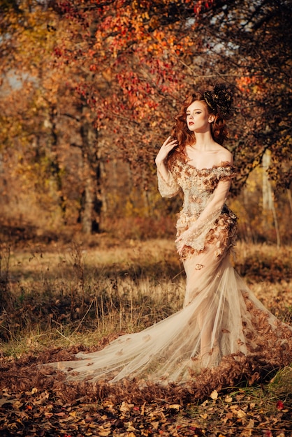 노란 단풍과 쉬폰 드레스의 가을 숲에 서있는 아름다운 우아한 여자