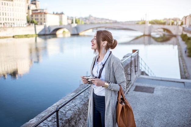 Bella ed elegante donna con macchina fotografica che si gode la città mattutina in piedi vicino al fiume nella città vecchia di lione