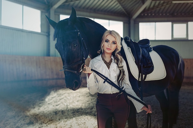 Beautiful elegant young blonde girl standing near her horse dressing uniform competition