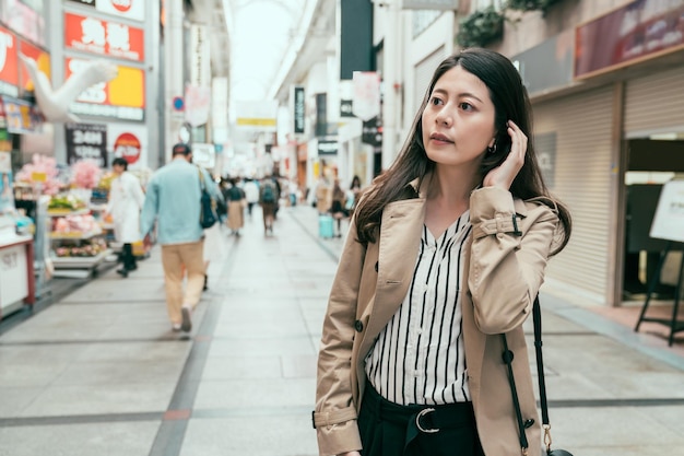 Beautiful elegant young girl with long hair wearing spring coat walking on city street in casual style. lady shopping and buying souvenir in business trip. woman looking curiously in shinsaibashi