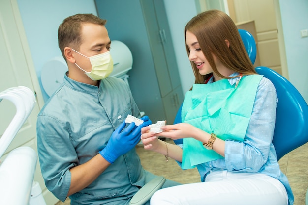 Foto bella ragazza emotiva che si siede in una sedia dentale accanto a un medico maschio. clinica dentale. dottore e paziente