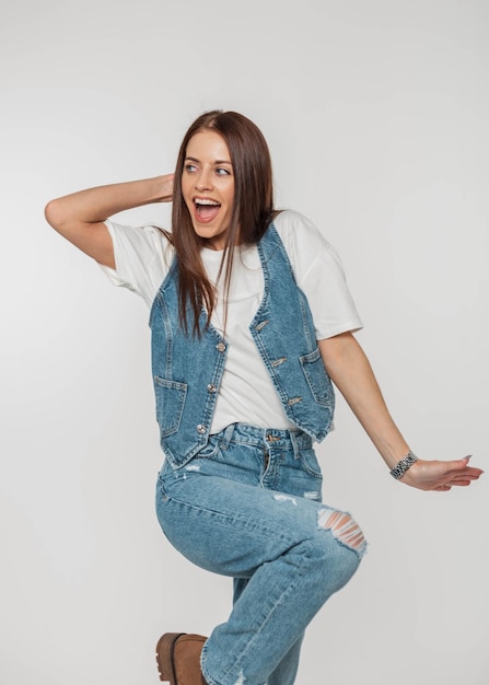 Premium Photo  Beautiful emotional positive woman with funny emotions in  fashionable denim outfit with a jeans vest white tshirt and jeans on a  white background in the studio