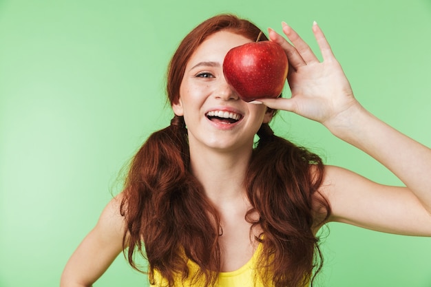 아름 다운 감정적인 젊은 빨간 머리 소녀 사과와 녹색 벽 배경 위에 고립 된 포즈.