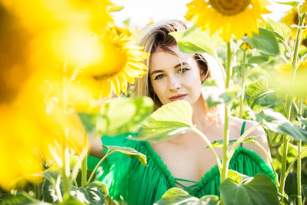 Beautiful european girl in a green dress on nature with sunflowers