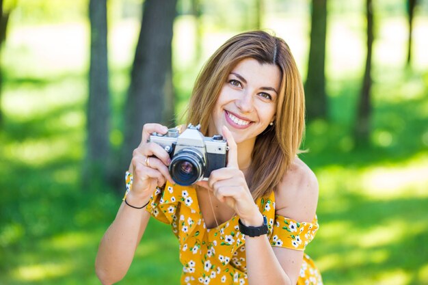 Beautiful european girl in a yellow dress with a retro camera in the morning park