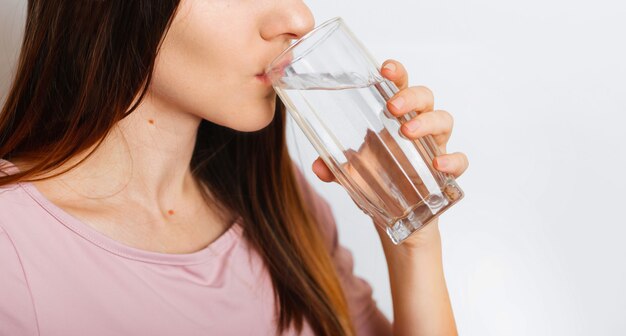 Beautiful european race ukrainian young girl women drinks water from glass on grey