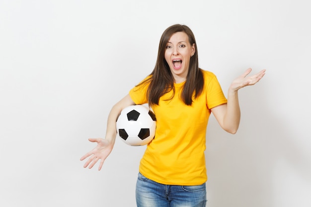 Красивая европейская молодая сердитая кричащая женщина, футбольный фанат или игрок в желтой форме, держащая футбольный мяч на белом фоне. Спорт, играть в футбол, здоровье, концепция здорового образа жизни.