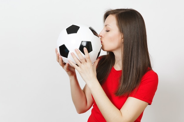 Beautiful european young cheerful happy woman, football fan or\
player in red uniform hold kiss classic soccer ball isolated on\
white background. sport play football, health, healthy lifestyle\
concept.