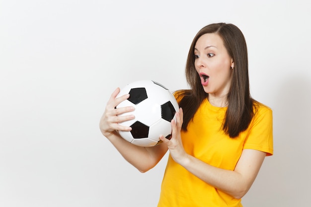 美しいヨーロッパの若い陽気な幸せな女性、サッカーファン、または白い背景で隔離のサッカーボールを保持している黄色の制服を着たプレーヤー。スポーツ、サッカー、健康、健康的なライフスタイルのコンセプト。