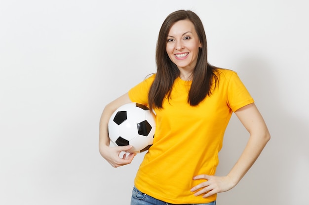 Beautiful European young cheerful happy woman, football fan or player in yellow uniform holding soccer ball isolated on white background. Sport, play football, health, healthy lifestyle concept.