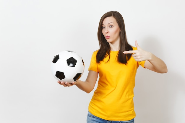 Beautiful european young cheerful happy woman, football fan or\
player in yellow uniform pointing on soccer ball isolated on white\
background. sport, play football, health, healthy lifestyle\
concept.